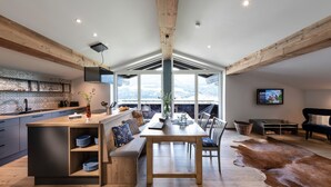 Eine moderne Küche mit einer Holztheke, eine Essecke mit großem Tisch und ein Wohnbereich mit Sofa und Fernseher.