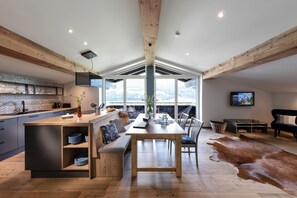 Ett modernt kök med en köksö i trä, en matplats med ett stort bord och ett vardagsrum med soffa och TV.
