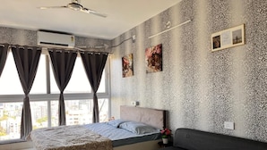 Ein Schlafzimmer mit einem Bett, einem Sofa, einem Fenster mit Vorhängen, einer Wandklimaanlage und gerahmten Bildern.