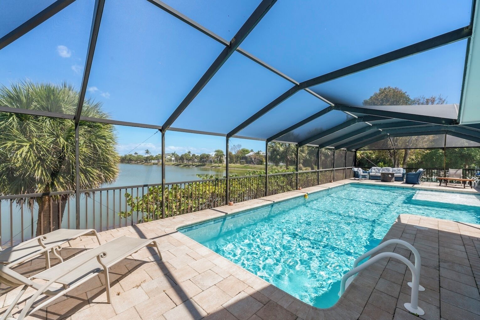 A covered outdoor swimming pool with a view of a lake and palm trees.