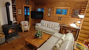 A log cabin interior with a fireplace, sofa, television, and wooden walls.