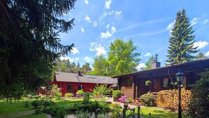 A wooden cabin with a red roof, a pond, and a dog in the foreground.