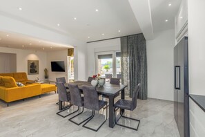 A modern living room with a yellow sofa, a dining table with chairs, a flat-screen TV, and a large window with curtains. - Villa Mirela - Perfect Family escape With  Private Pool, BBQ & Fenced Yard (Šišan)