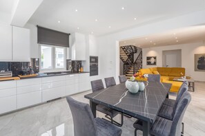 A modern kitchen with white cabinets, a dining area with a marble table, and a yellow sofa. - Villa Mirela - Perfect Family escape With  Private Pool, BBQ & Fenced Yard (Šišan)