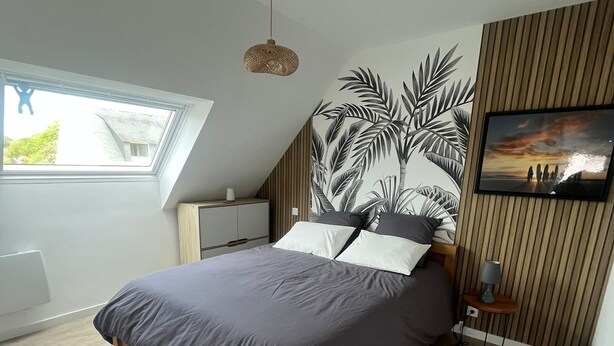 Ein Schlafzimmer mit einem Bett, einem Nachttisch, einer Lampe, einem Wandbild und einem Fenster.