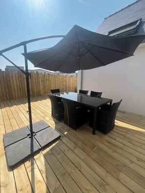 Eine Terrassengruppe mit Tisch und Stühlen, einem großen Sonnenschirm und einem Holzdeck.