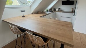 Eine moderne Küche mit einem großen Holztisch, zwei Korbstühlen, einem Oberlicht und Blick auf Häuser.