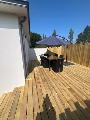 Eine Holzterrasse mit Tisch und Stühlen, einem violetten Sonnenschirm und einem Holzzaun im Hintergrund.