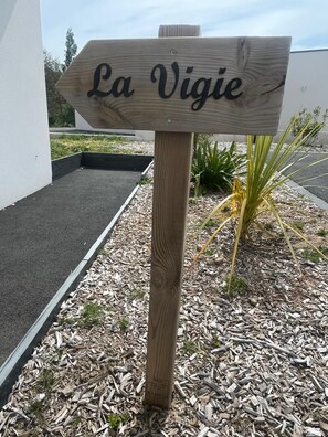 Une pancarte en bois portant l’inscription « La Vigie », placée dans un espace paysager agrémenté de paillis et de plantes.