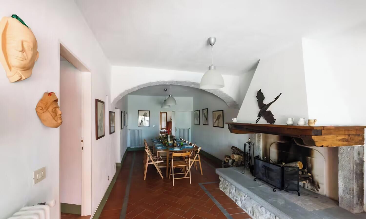 A dining area with a long table, chairs, and a fireplace with a bird sculpture.