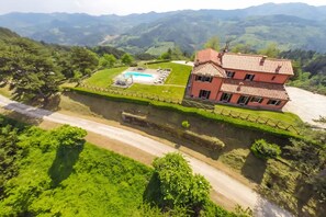 Ein zweistöckiges Haus mit Schwimmbad, umgeben von üppiger Vegetation und Bergen.