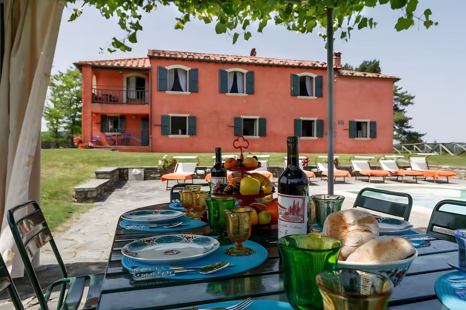 An outdoor dining area with a table set for two, a bottle of wine, and a fruit bowl.