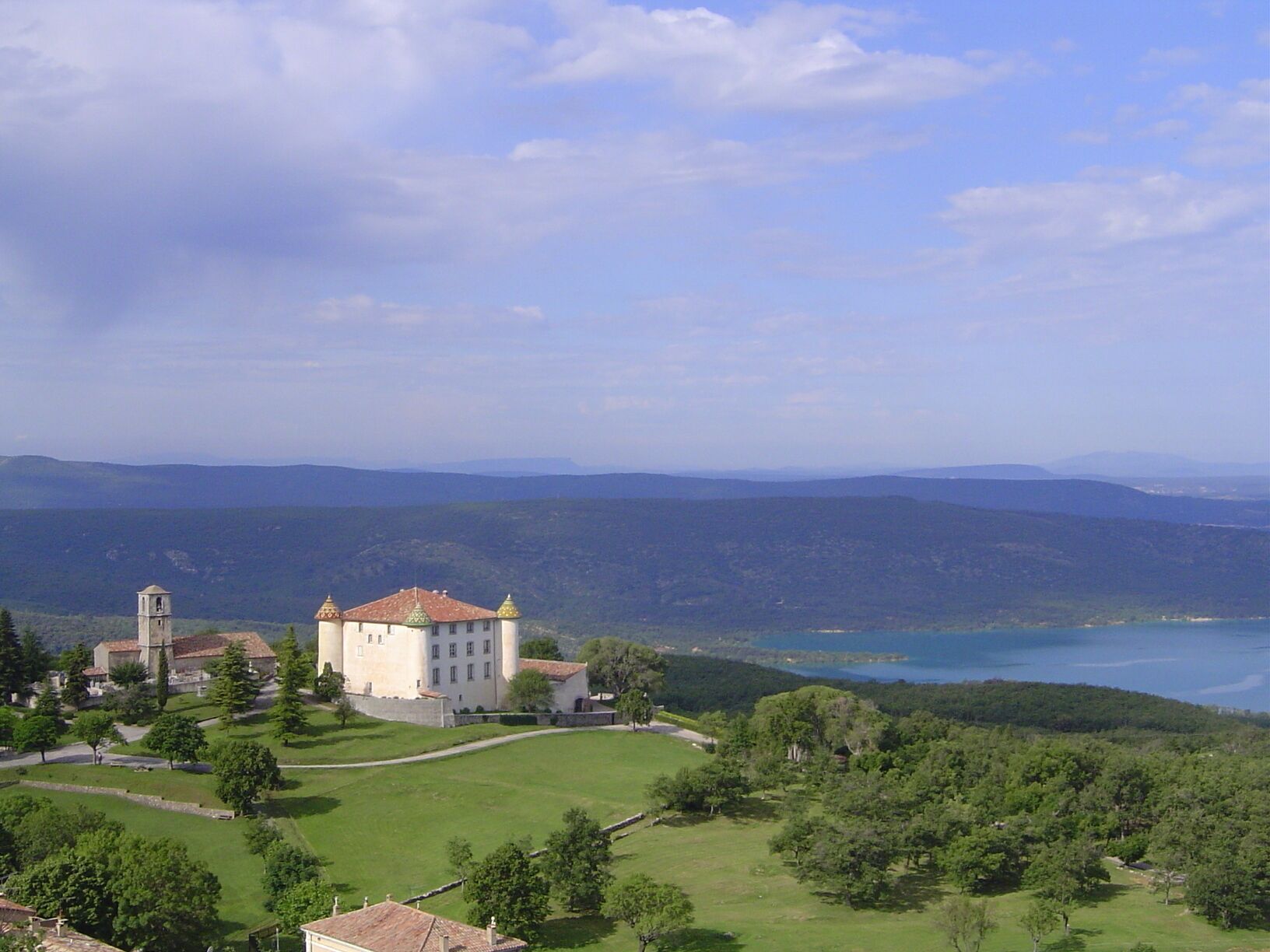 A historic building with a bell tower, surrounded by lush greenery and a lake.