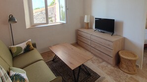 Sala de estar com sofá, televisão em móvel de madeira, mesa, abajur e janela com vista.