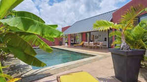 Et poolområde med pool, stole og en bygning med rød facade og metal tag.