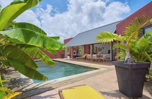 A poolside area with a pool, chairs, and a building with a red exterior and a metal roof. - Villa Coco Chic- Private pool - Tropical garden (Pointe aux Piments)
