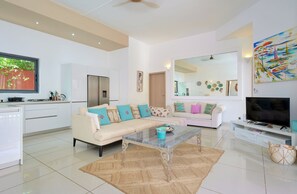 A modern living room with a sofa, coffee table, TV, and kitchen area. - Villa Coco Chic- Private pool - Tropical garden (Pointe aux Piments)