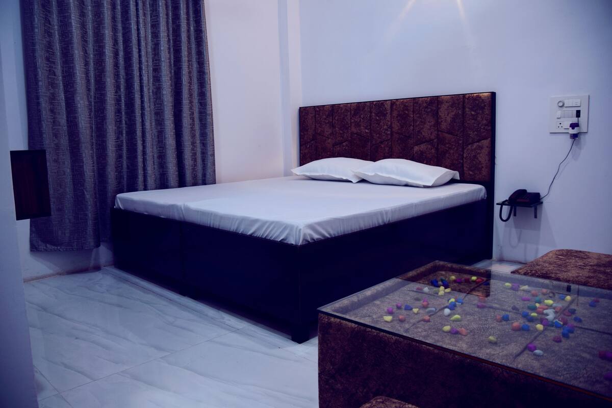 A bedroom with a bed, a bedside table, a wall socket, and a curtain.
