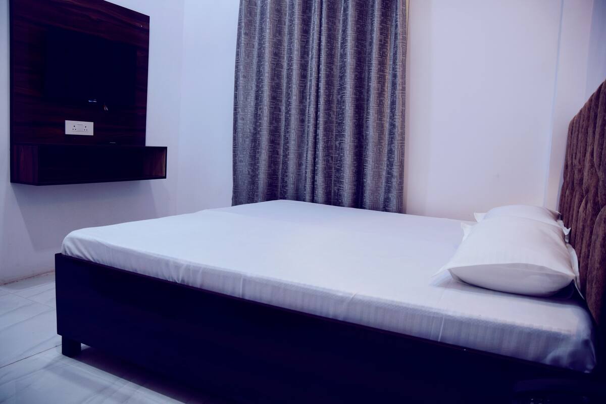 A bedroom with a bed, a TV mounted on the wall, and a curtain.