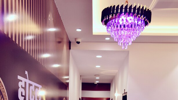 Corredor de hotel com um candelabro moderno, uma parede com texto em hindi e uma área de estar.