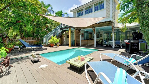 Ein Poolbereich mit Liegestühlen, einem Grill und einer überdachten Terrasse.