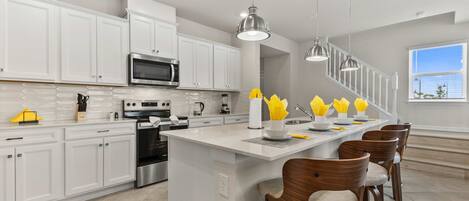 A modern kitchen with white cabinetry, stainless steel appliances, and a central island with bar stools.
