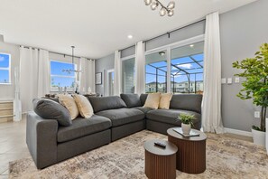 Ein modernes Wohnzimmer mit einem Ecksofa, zwei runden Couchtischen und einem großen Fenster mit Vorhängen.