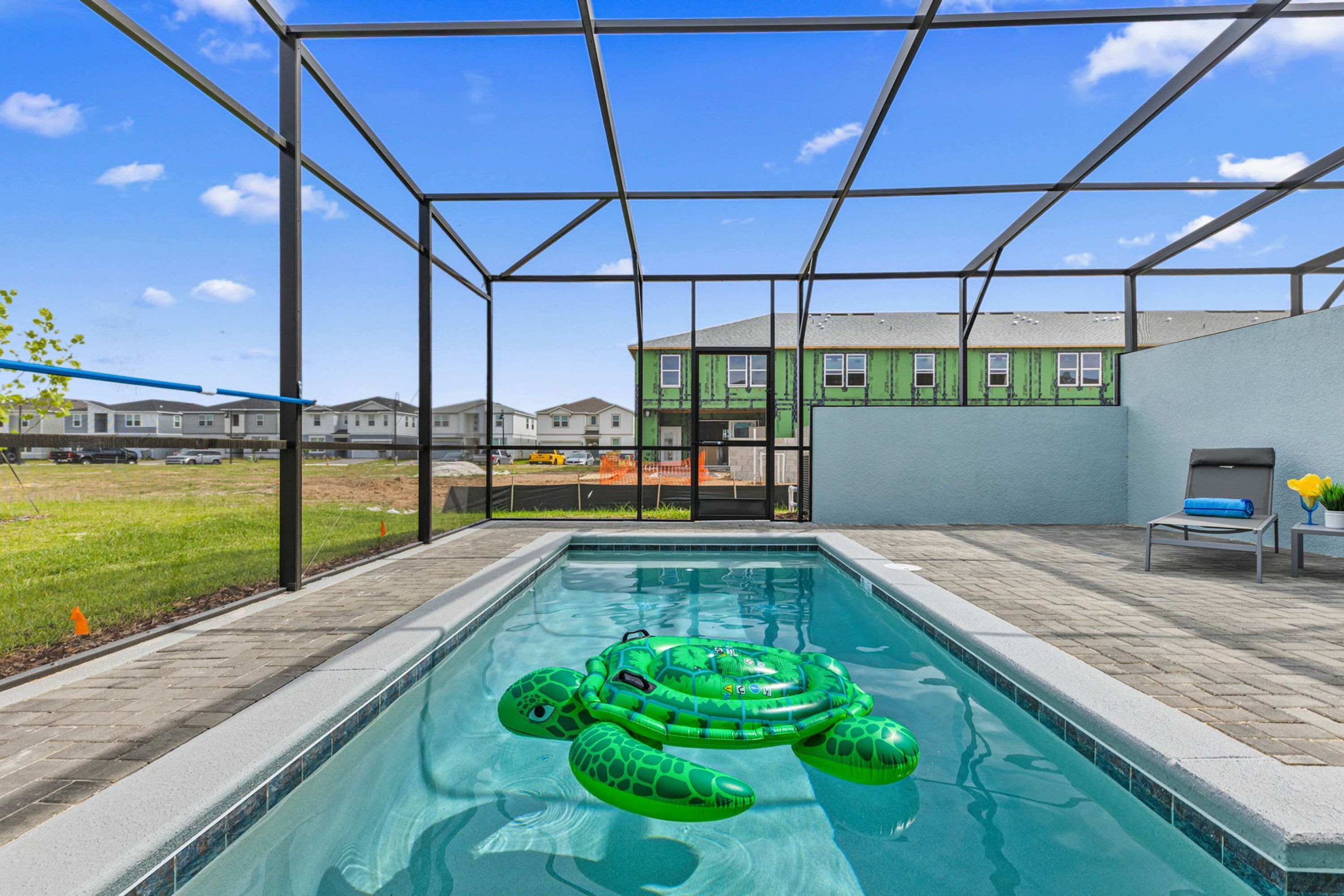 A swimming pool with a green inflatable turtle, a covered patio area, and a view of a building with green siding.
