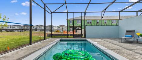 A swimming pool with a green inflatable turtle, a covered patio area, and a view of a building with green siding.