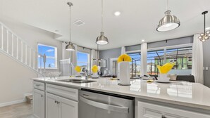 Una cocina moderna con armarios blancos, electrodomésticos de acero inoxidable e iluminación colgante.
