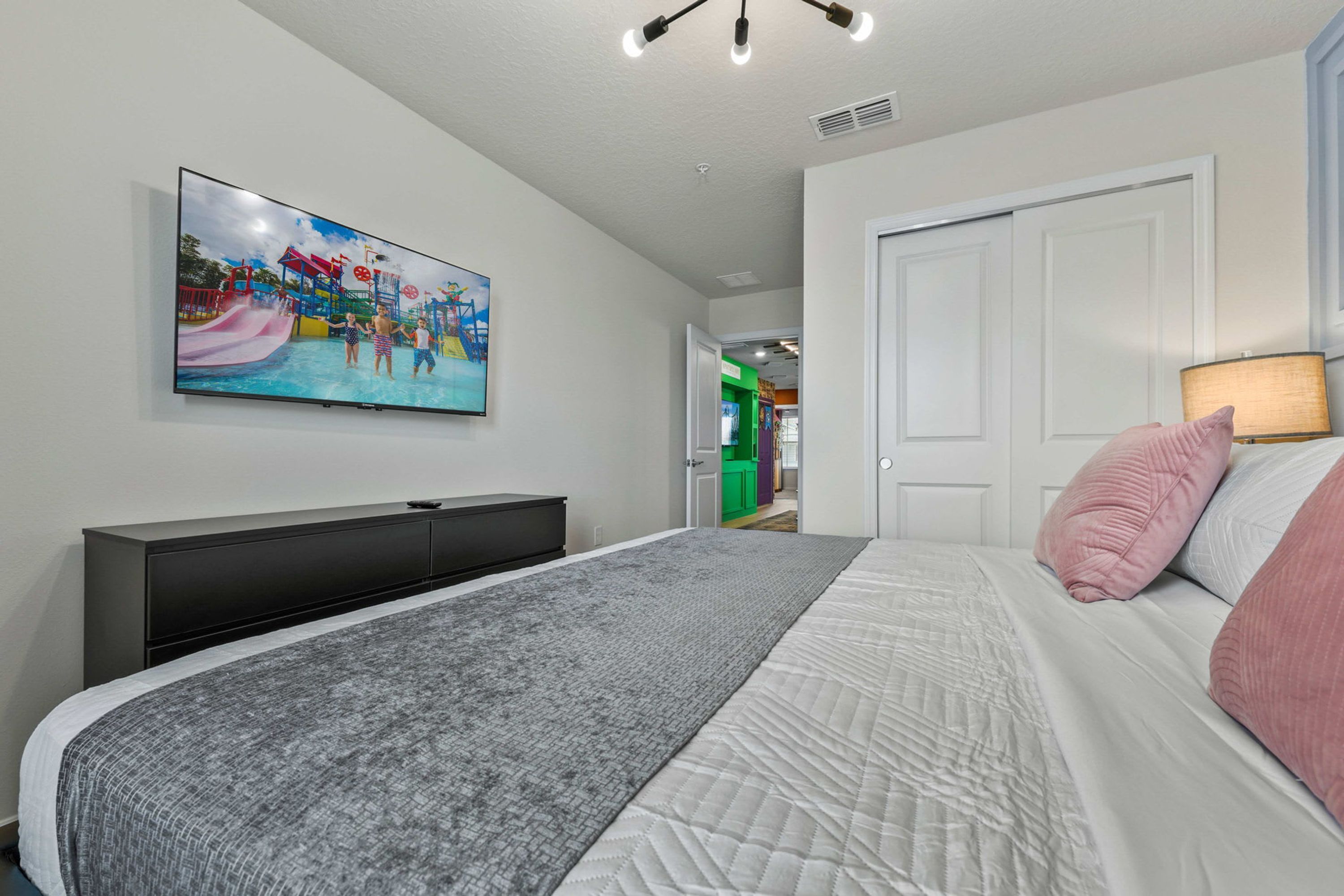 Un dormitorio con una cama, un televisor montado en la pared, una puerta y una lámpara.