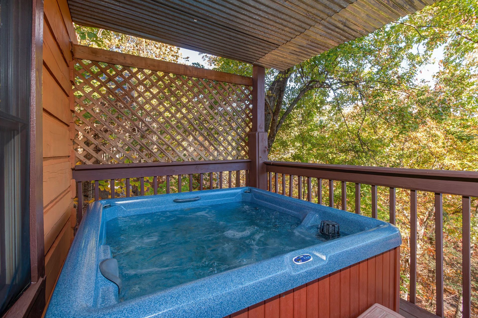 A hot tub on an outdoor deck with a wooden lattice backdrop and a view of trees.