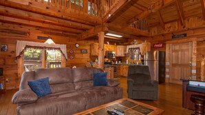 L’intérieur d’une cabane en rondins, avec un canapé, un fauteuil et une table basse sur laquelle reposent des télécommandes.