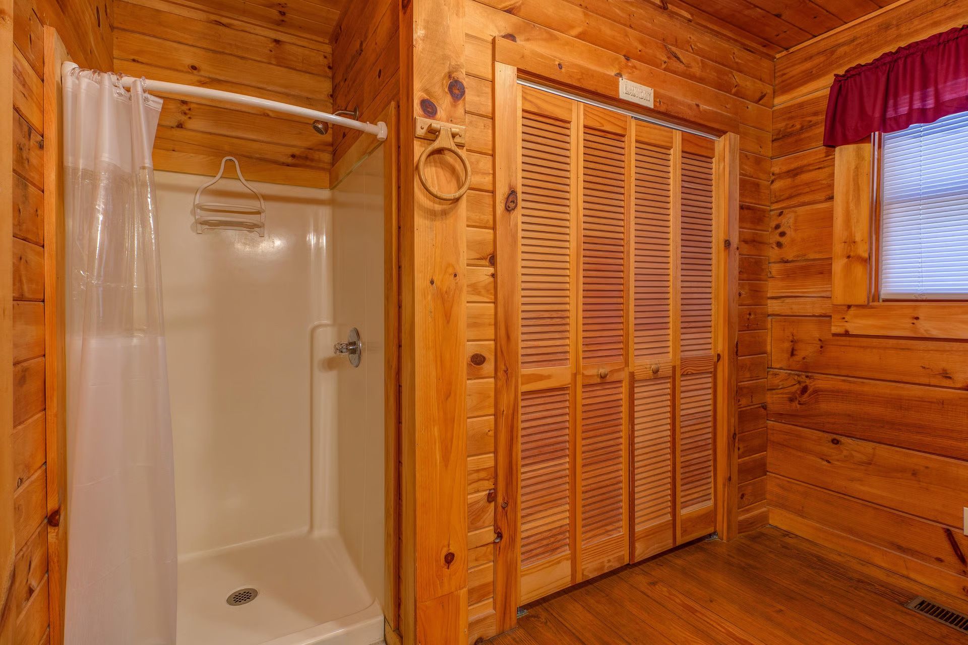 A wooden cabin with a shower, a wooden door, and a window with blinds.
