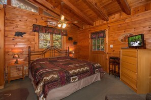 A wooden cabin bedroom with a bed, two windows, a ceiling fan, a TV, and a dresser. - Sky Harbor| Pet Friendly | Hot Tub | View | WiFi (Sevierville)