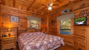 Une chambre dans une cabane en bois, avec un lit, une commode, des tables de chevet et un ventilateur de plafond.