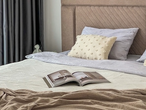 A neatly made bed with a magazine, pillows, and a textured headboard.