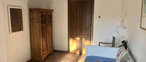 A room with a bed, a wardrobe, and a door leading to another room.
