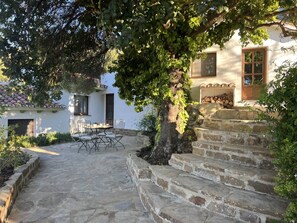 Una escalera de piedra que conduce a un edificio blanco con tejado de baldosas, una mesa con sillas y un árbol de hojas verdes.