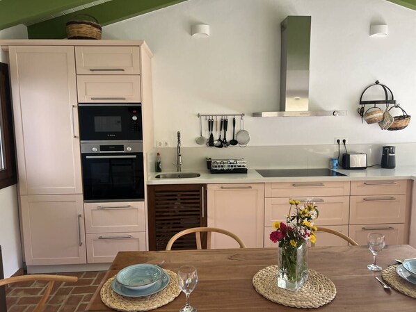 A kitchen with a dining table set for two, a vase with flowers, and a toaster on the countertop.