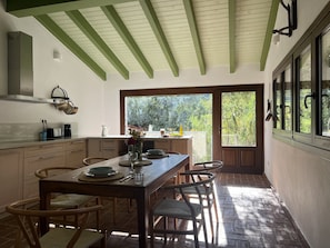 A kitchen with a wooden table and chairs, a large window, and a view of greenery outside.