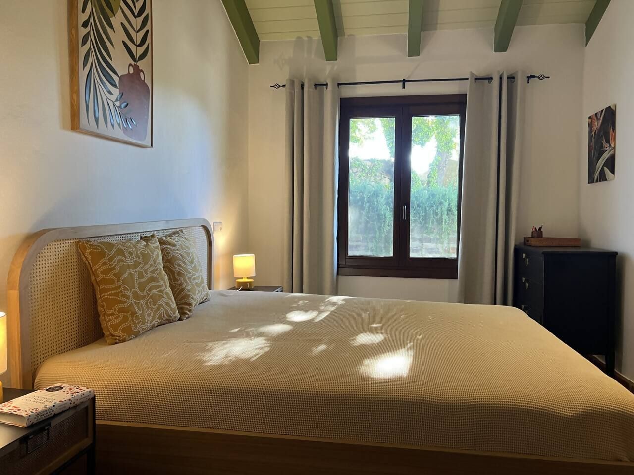 Un dormitorio con cama, mesitas de noche, una ventana con cortinas y una obra de arte colgada en la pared.