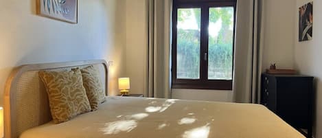 A bedroom with a bed, bedside tables, a window with curtains, and a wall-mounted artwork.