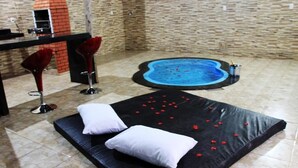 A room with a black mattress, two white pillows, a small pool with red flowers, and two red bar stools. - Motel hotel Vitória  (Rialma)