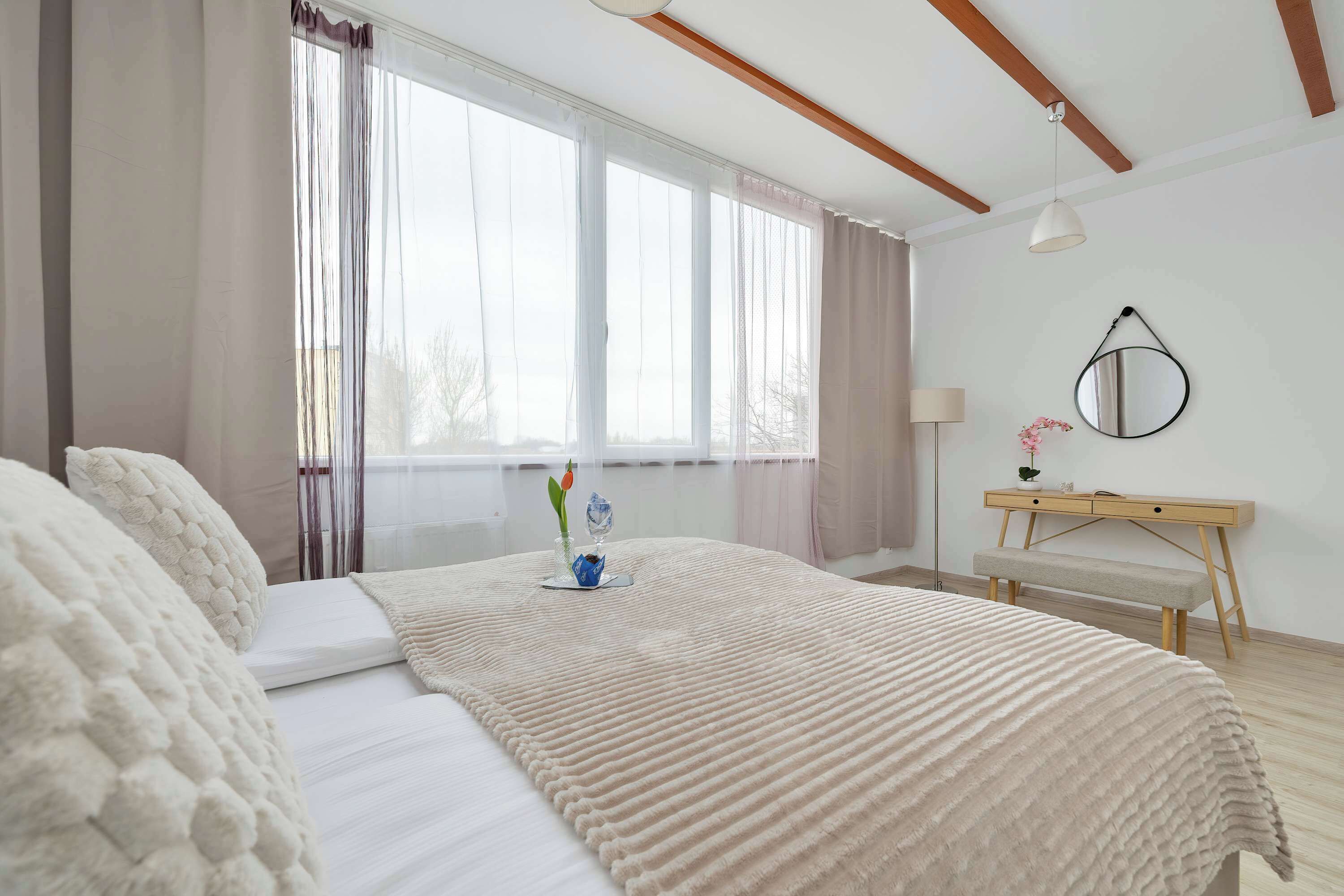 A bedroom with a bed, bedside table, lamp, and window with curtains.
