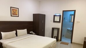 Une chambre d’hôtel avec un grand lit, une armoire, une table de chevet avec un téléphone, un tableau encadré au mur et une salle de bain visible à travers une porte ouverte.