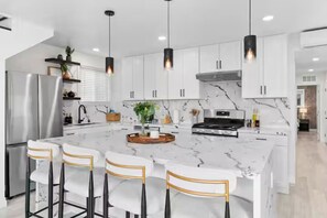 A modern kitchen with white cabinets, a marble island, stainless steel appliances, and pendant lighting. - The Perch by Coastline Vacation Rentals (San Diego)
