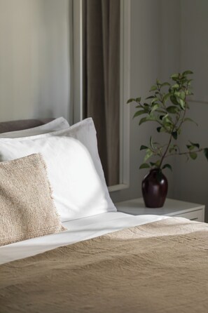 A bed with white linens, a burlap pillow, and a dark vase with a plant. - Spacious villa with beautiful large garden (NEA MOUDANIA)