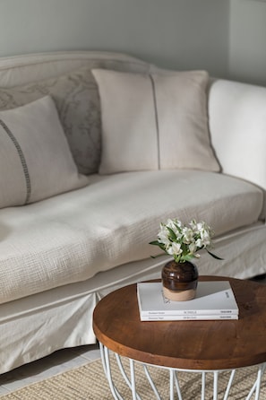 A sofa with a cushion, a round wooden table with a book, and a vase with flowers. - Spacious villa with beautiful large garden (NEA MOUDANIA)