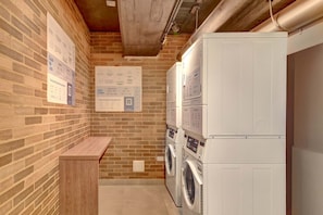 A laundry room with brick walls, a wooden bench, and stacked washing machines. - w Premium Loft in the Heart of Bogot (Bogotá)
